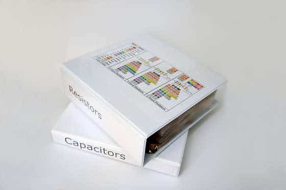 White binder with labeled sections for resistors and capacitors on plain background.