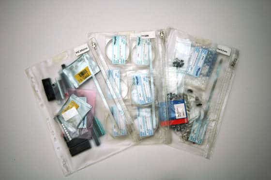 Clear plastic bags containing various small parts, tools, and possibly instructions or labels, arranged in a fan shape.