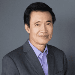 Man in dark grey suit jacket and light blue shirt on a gray background.