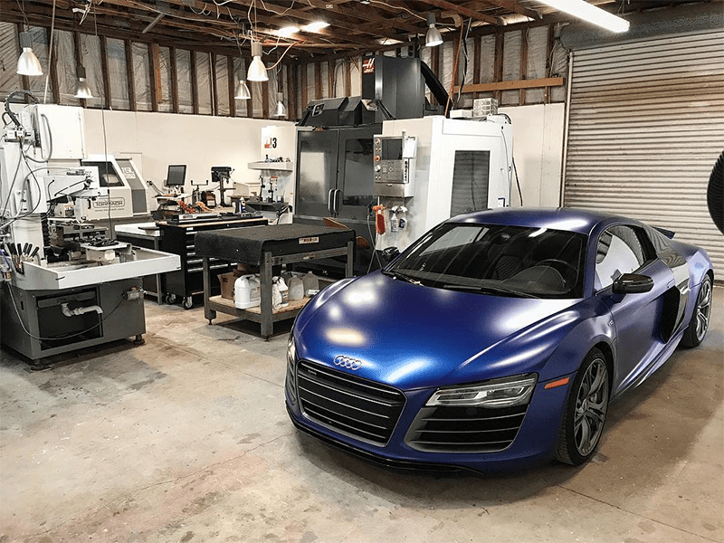 A workshop with machinery, tools, and a blue Audi R8 car.