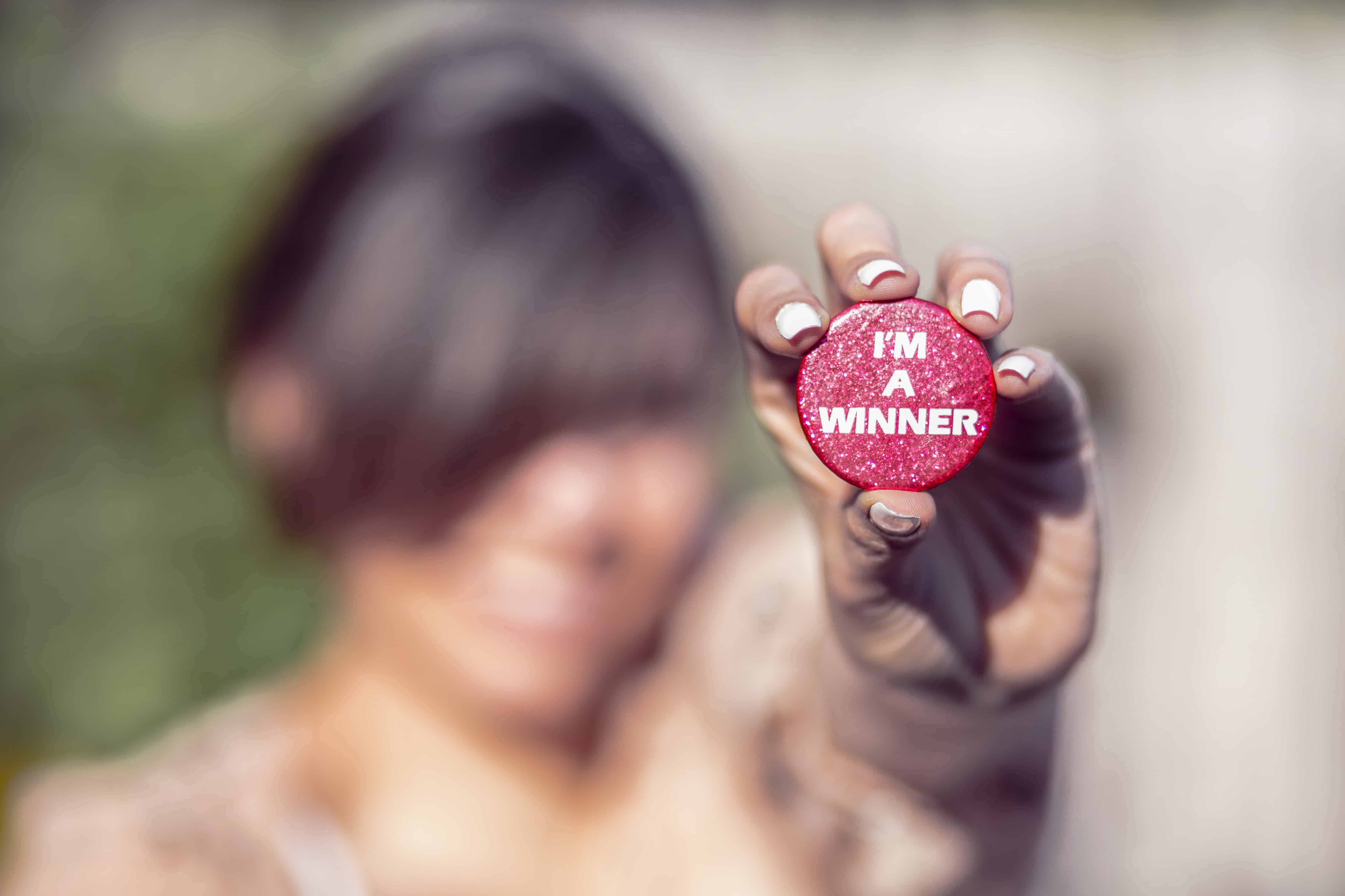 A woman holding a pink button with "I'M A WINNER" text.
