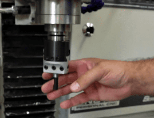 Metal component with three holes on workbench near CNC machinery.