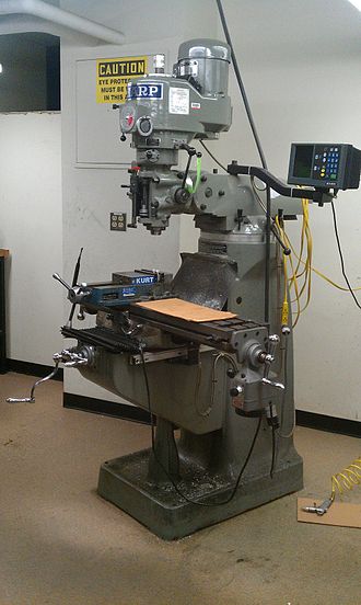 A large gray 3-axis milling machine with vertical column and table in an industrial setting.