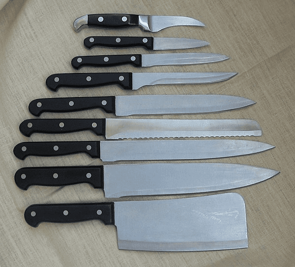 Black-handled kitchen knives with silver blades arranged on light-colored wooden surface.