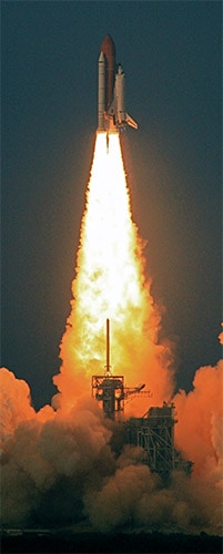 A white rocket with a red tip blasts off into a dark blue sky, surrounded by flames and smoke.