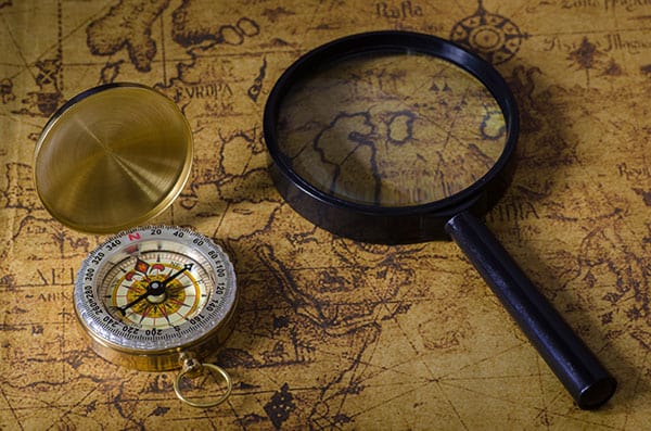 Antique brass compass with magnifying glass on vintage yellowed map.