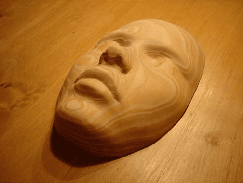 A wooden carving of a human face on a light-colored wood surface.