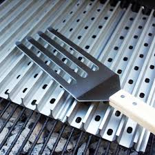 A metal grill brush with wooden handle on top of a metal grate, featuring long thin bristles angled for cleaning.