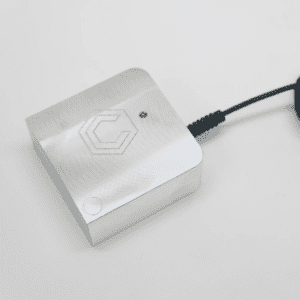 Small white device with black cord and circular indentation, set against a light gray background.