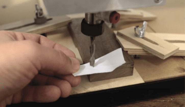 A hand holding a piece of paper near a tool on a wooden machine.