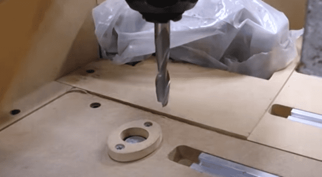 Drill bit partially inserted into wooden material with surrounding tools and materials.