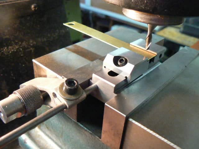 Metalworking vise with sine bar attached to milling machine.