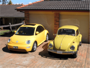 A yellow Volkswagen Beetle and a yellow model next to a garage.