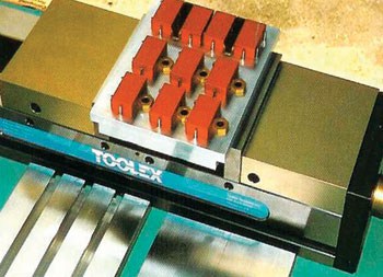 Metal tool with "TOOL" label and rectangular shape, featuring multiple small holes on a flat top surface in a workshop background.