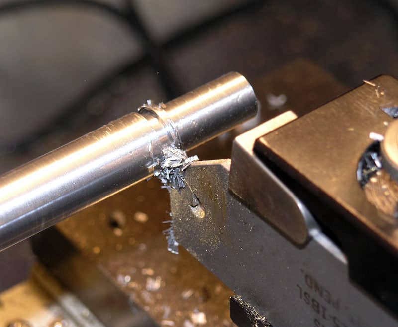 Metal object being machined on a lathe, showing metal shavings and detailed cutting process.