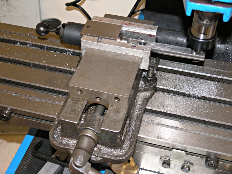 Metalworking vise on milling machine table with slotted ways and T-handle.