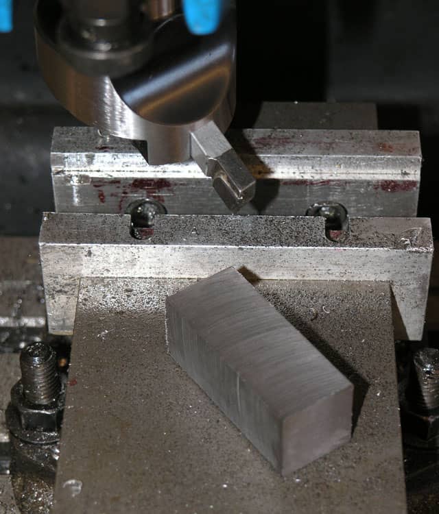 Metal workbench with rectangular metal block, drill press, lathe, and miscellaneous tools and equipment.