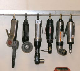 A collection of air tools suspended on a metal bar.
