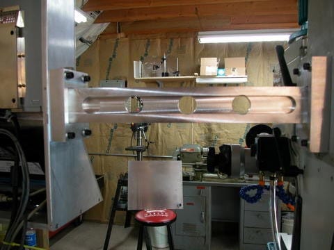 A well-lit workshop with machinery and tools, including a large metal frame and various equipment scattered throughout.