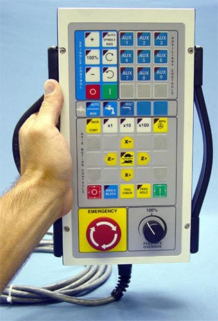 A hand grasping a milling machine control panel with buttons, switches, and a digital display showing tool information.