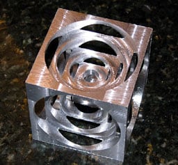 Metallic cube with intricate circular cutouts.