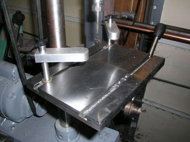 Metalworking machine with L-clamp and cylindrical pieces on a gray metal surface.