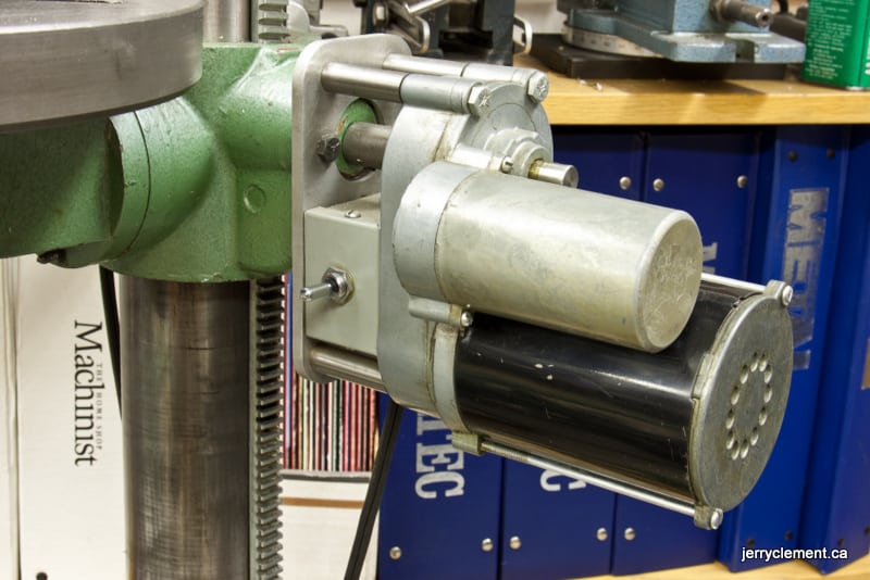 Green metal column with silver cylinder on wooden table in workshop setting.