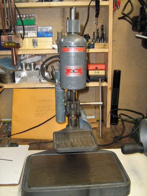 Gray metal electro-sensing press in workshop with tools and attachments.