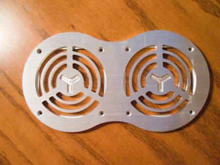 A silver metal fan cover with two concentric circles and a central "Y" shape, mounted on a wooden surface.
