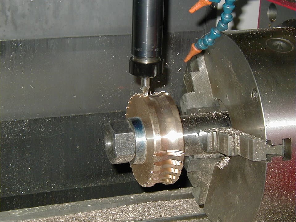 A milling machine spindle with a 4th axis and cutting tool on a metal component.