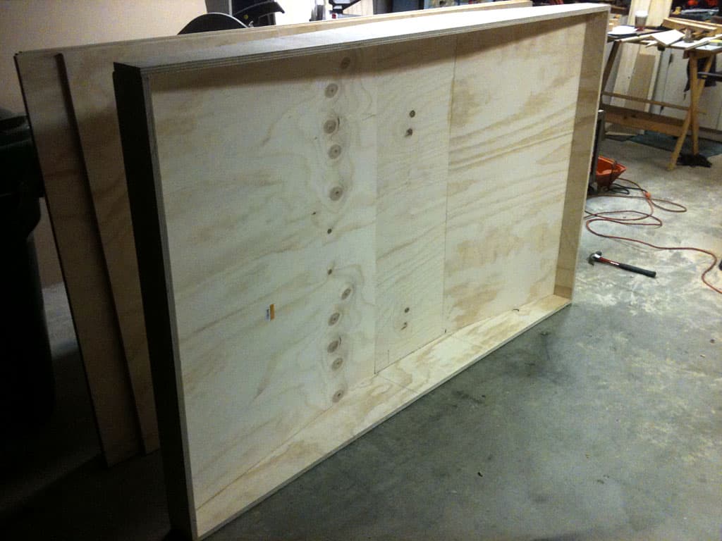 Large unfinished plywood board leaning against workshop wall.