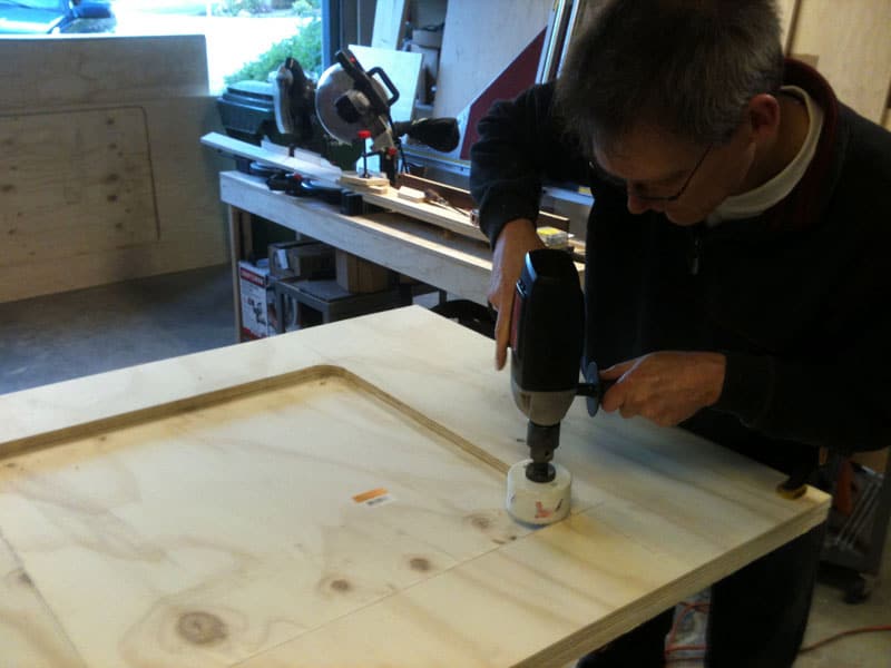 Man using drill on wooden board in a machinist's workspace.