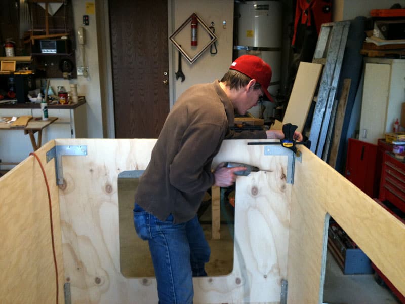 Man in garage workshop using clamps on wooden boards, surrounded by machine shop and metal fabrication tools.