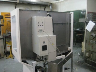 Large white machine in workshop with buttons and controls, surrounded by tools and equipment.
