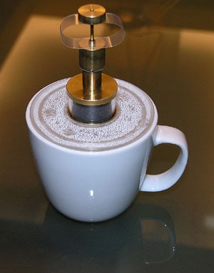 A white coffee mug with a metal object protruding from its top against a brown background.