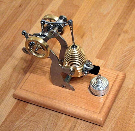 Mechanical device on wooden base with metallic composition featuring gold and silver hues.