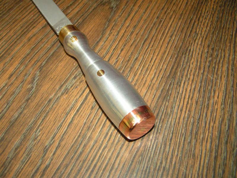 A silver-handled chisel with copper cap against a wooden background.