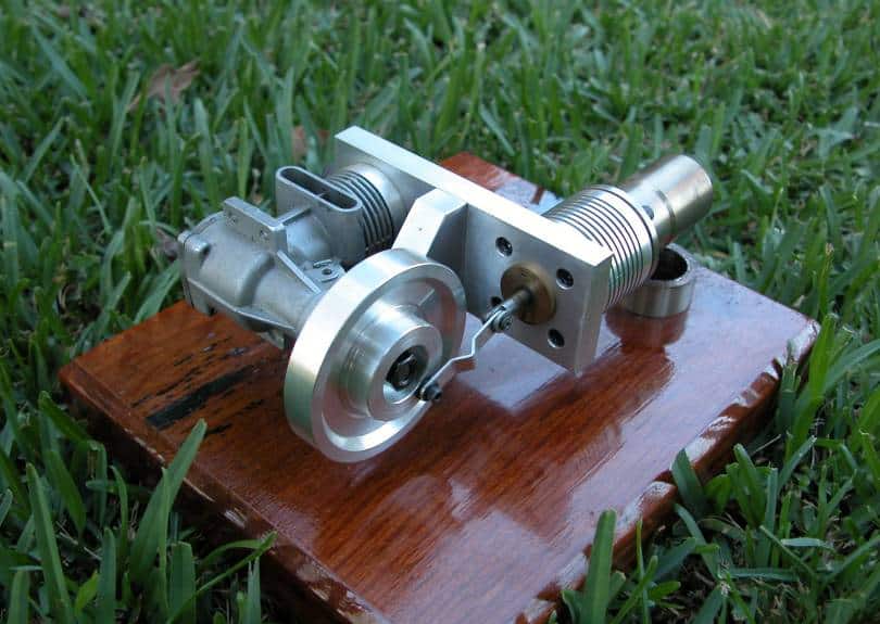 Small intricately designed metal mechanism on a wooden platform amidst lush greenery.