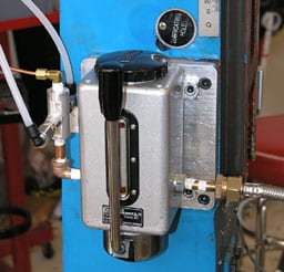 Silver metal box with black handle, mounted on blue wall, connected to white and copper hoses.