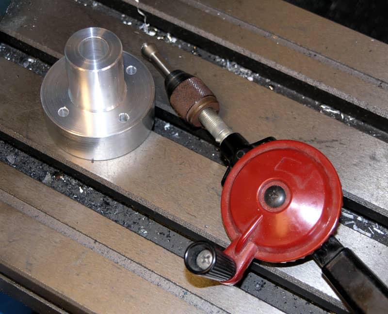 Red hand drill on metal workbench beside aluminum object.