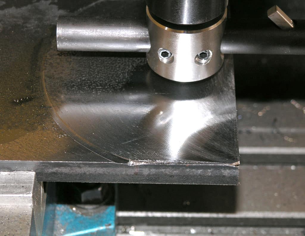 Metal cutting tool or machine part, shiny silver metal surface with scratches and marks in a workshop setting.