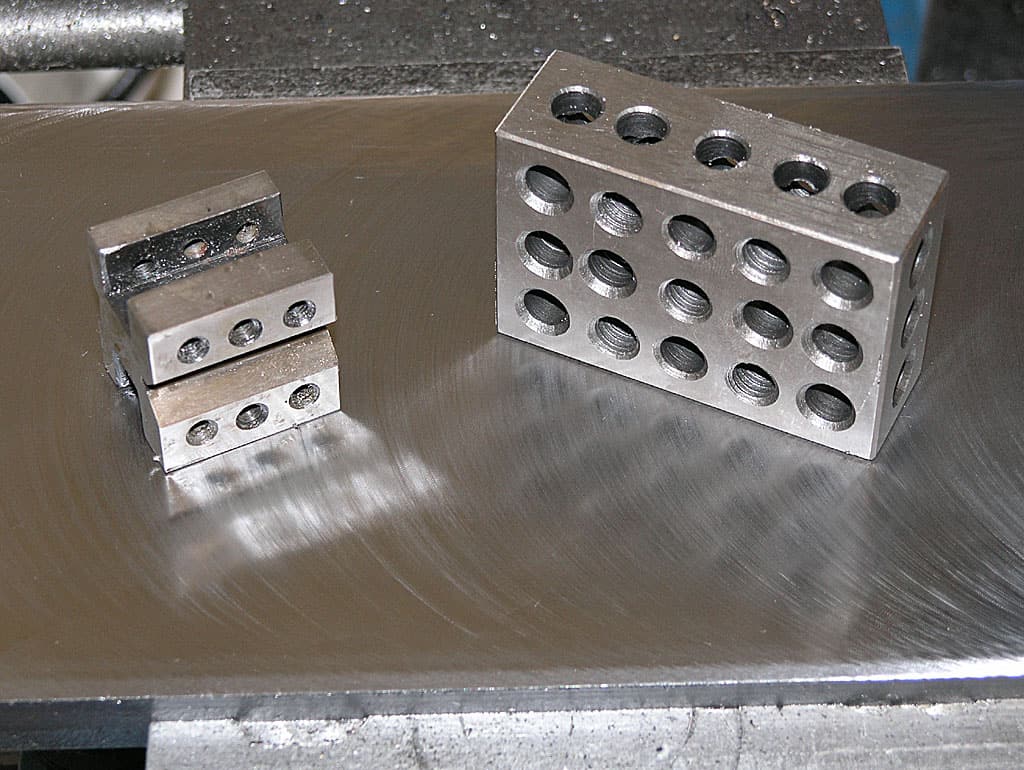 Metal blocks with holes drilled into them on a metal surface.