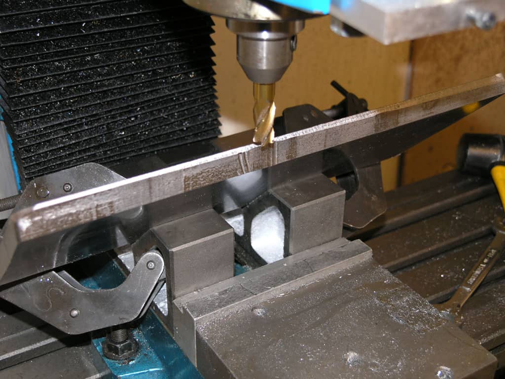 A machinist's workspace with a drill press, cutting tool, and clamped metal block.
