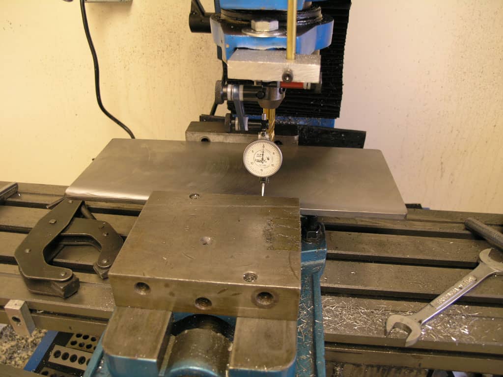 Metalworking machine with dial indicator on table, surrounded by tools and equipment.