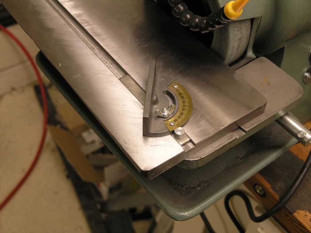 Gray table saw angle adjustment mechanism with metal plate and yellow dial.