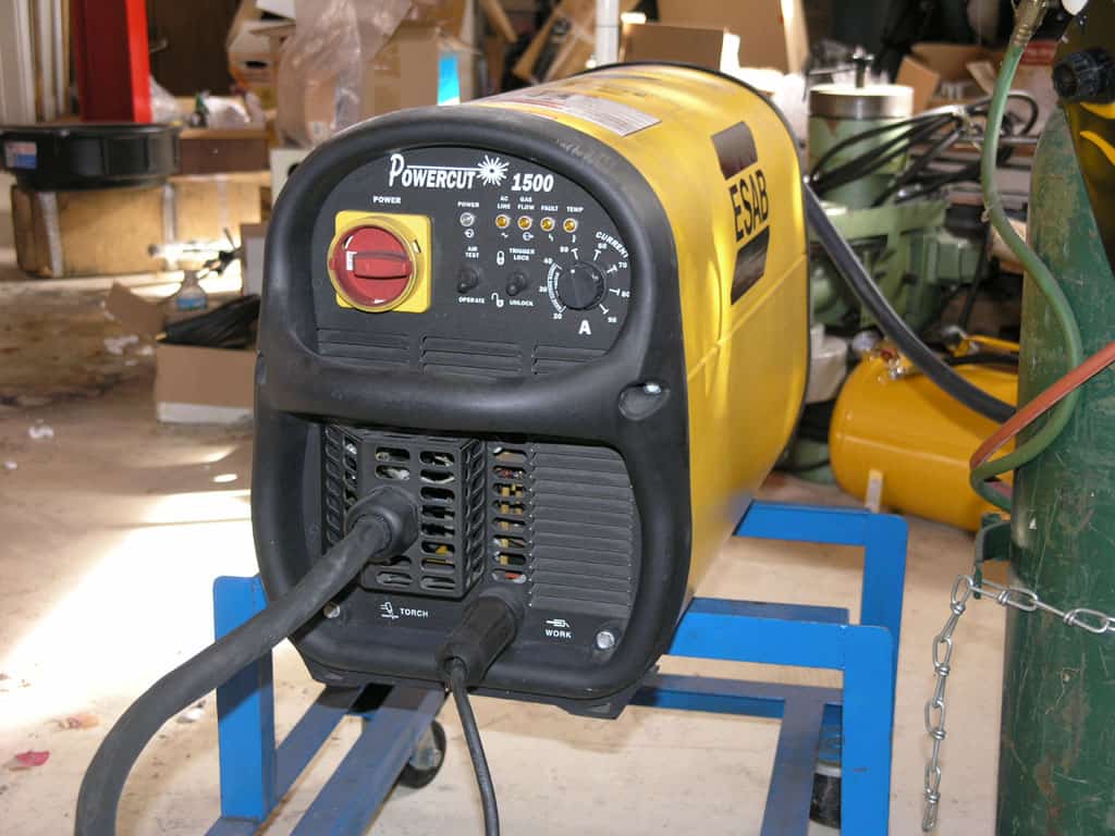 A yellow and black Powercut 1500 welder on a blue stand in a cluttered workshop or garage.