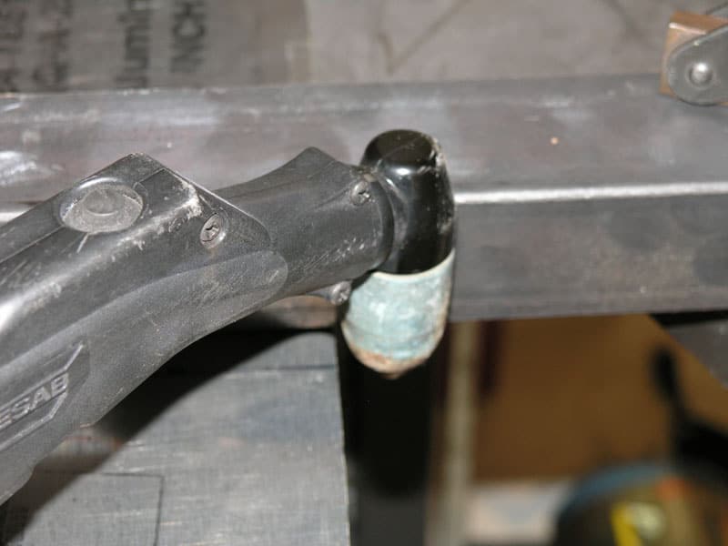 Metal object with black handle and light blue cylinder on gray workbench.