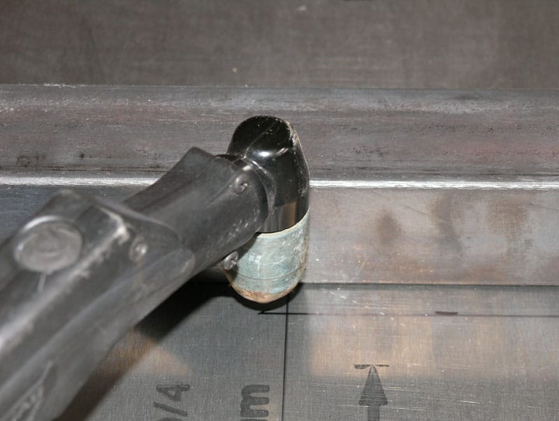 Black vacuum hose with green tape wrapped around end, on gray surface near metal/concrete wall.