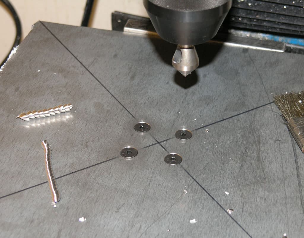 Metalwork on a bench with drilling machine and metal tools and parts.