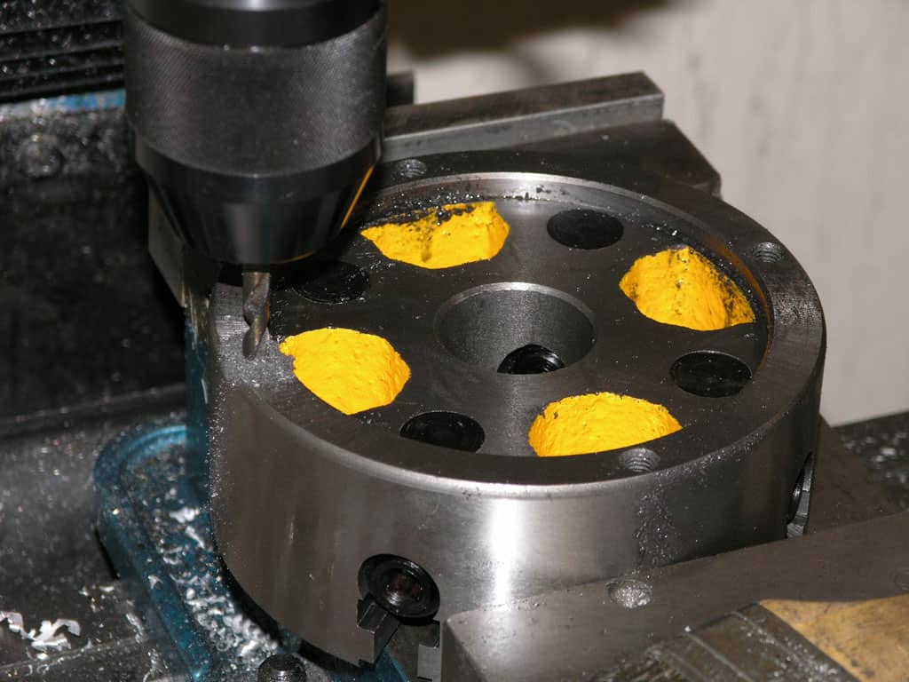 Black metal object with yellow material inside, multiple holes, on dark surface.